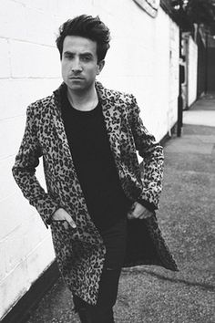 a man standing next to a white wall wearing a leopard print coat and black pants