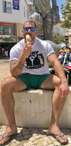 a man sitting on a wall eating an ice cream cone in front of a statue