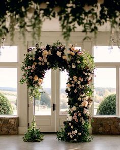 an archway decorated with flowers and greenery in front of two large windows, overlooking the countryside