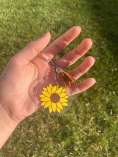 a person's hand holding a yellow flower shaped keychain in the grass