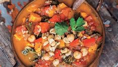 a bowl filled with vegetables and beans on top of a wooden table next to a spoon