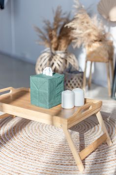 a wooden tray with two candles and a green bag on it in front of some chairs