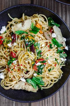 pasta with spinach and feta cheese in a black bowl on a wooden table