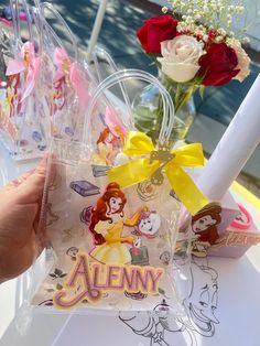 someone is holding up some disney princess themed candy in front of flowers and candles on a table