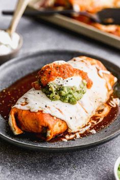 a black plate topped with enchiladas covered in sauce