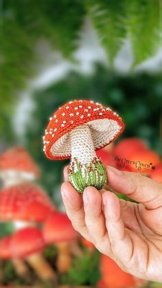 a hand holding a tiny red mushroom in front of some green plants and orange flowers