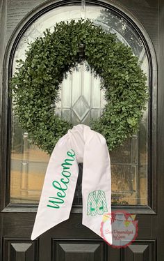 a green wreath with the words welcome to me on it hanging from a front door