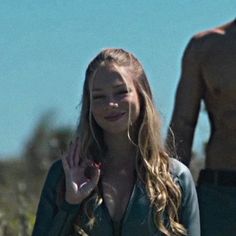 a woman with her hand up in the air while standing next to a man who has his shirt off