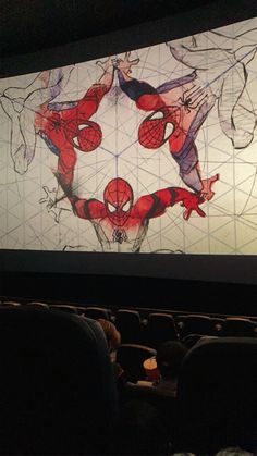 a large screen with spiderman on it in the middle of a movie theater filled with people