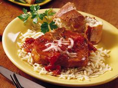 a yellow plate topped with meat covered in sauce and rice next to a knife and fork