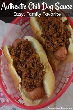 two hot dogs with chili on them sitting in a red basket next to each other