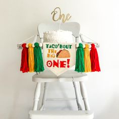 This Taco Bout the Big One 1st birthday highchair banner is the perfect fiesta flag decor to celebrate your little one who is turning a year old. A taco is surrounded by the words "Taco Bout the Big One" in bright red, green and gold font. It makes this flag a classic for their first celebration. Banner includes 6 tassels in green, gold and red separated by wooden beads. Hang on a high chair or above the cake table and when the party is over hang on the wall as part of a room decoration.  This c First Fiesta Table Decor, 1st Birthday Taco Theme, Taco About One Birthday Party, Taco 1st Birthday Party Boy, 1st Fiesta Theme Party Boy, Taco Bout One Birthday Party, My First Fiesta 1st Birthdays, First Fiesta Birthday Boy, Taco First Birthday