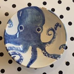 a blue and white plate with an octopus painted on it's side sitting on a polka dot surface