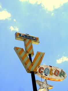 an old neon sign that is hanging off the side of a building in front of a cloudy blue sky