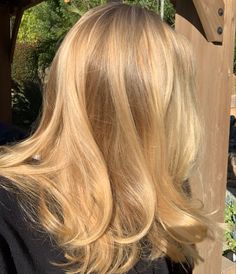 the back of a woman's head with long blonde hair in front of a wooden structure