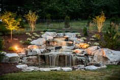 a small waterfall in the middle of a garden with lights on it's sides