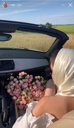 a woman sitting in the driver's seat of a car next to a bunch of flowers