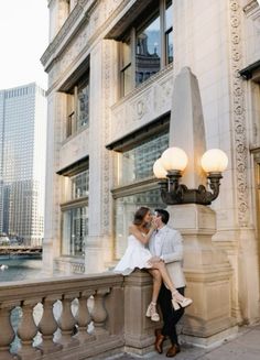 a man and woman are sitting on a ledge in front of a building with lights