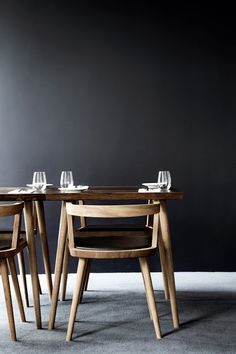 a table with four chairs around it in front of a gray wall and two empty wine glasses