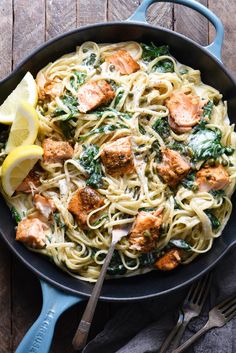 a skillet filled with pasta, meat and spinach on top of a wooden table