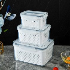 three plastic storage containers stacked on top of each other next to a vase with flowers