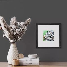 a vase filled with flowers next to two books and a framed photo on the wall