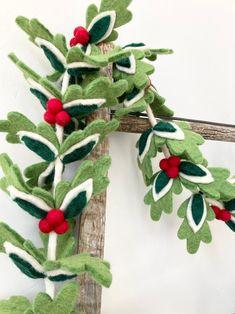 a green and white wreath with red berries hanging from it's sides on a wooden frame