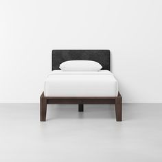 a bed with white sheets and black headboard against a white wall in an empty room