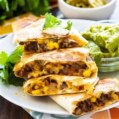 three burritos on a plate with guacamole and salsa in the background