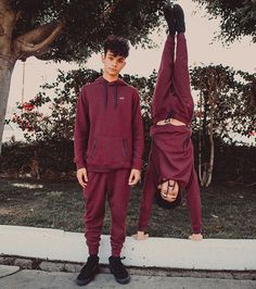 two young men standing in front of a tree doing handstands on the sidewalk