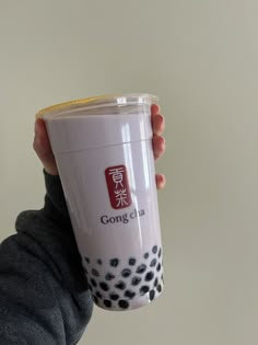 a person holding a plastic cup with writing on the side, in front of a white wall