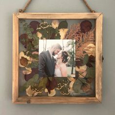 a wooden frame holding a photo of a bride and groom in front of leaves on the wall