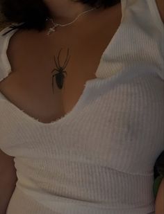 a woman with a spider tattoo on her upper arm and lower back breast, wearing a white top