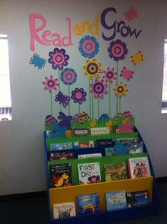 a book stand with books on it and flowers painted on the wall behind it that says read and grow