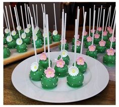 green cake pops with pink and white flowers on them sitting on a plate next to other desserts