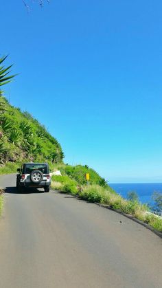 a car is driving down the road by the ocean on a clear day with blue skies