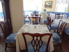 a dining room with blue and white table cloths on the tables, chairs and windows