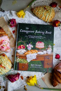 a cookbook sitting on top of a table with pastries and flowers around it