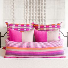 a bed with pink and orange pillows on it's headboard in front of a white wall