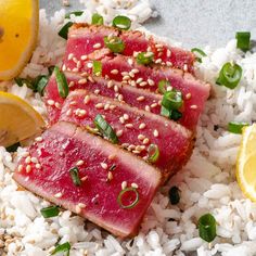 slices of tuna with sesame seeds on top of rice and lemon wedges next to it