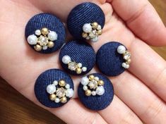 four blue buttons with white pearls and gold accents on their thumbnails are held in the palm of someone's hand