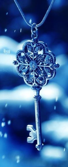 an ornate key hanging from a chain on a blue background with snow falling around it