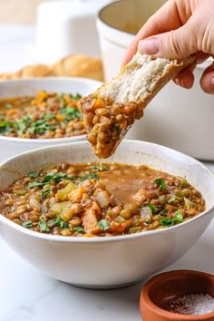 a person dipping a piece of bread into a bowl of soup