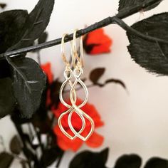 a pair of gold earrings sitting on top of a branch next to some red flowers