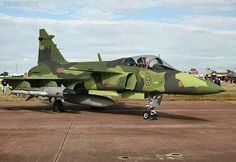 a camouflaged fighter jet sitting on top of an airport tarmac with people standing around it