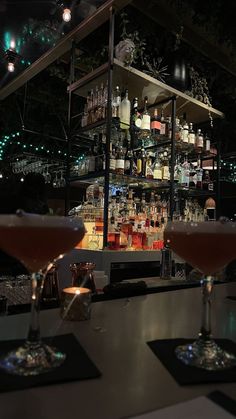 two martini glasses sitting on top of a bar filled with liquor bottles and drinks next to each other