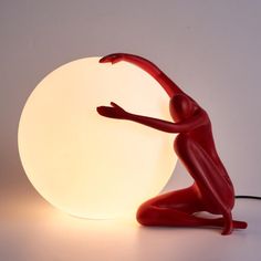 a red figurine sitting on the ground next to a light that is turned on