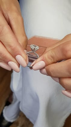 a woman holding onto a ring that is on top of her finger and it's being held by another person