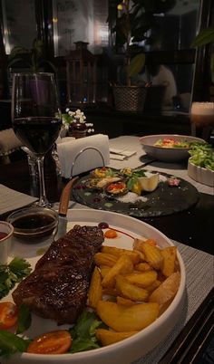 a steak dinner with fries and salad on a table in front of a glass of wine