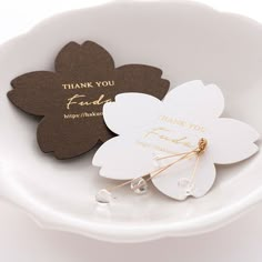 two flower shaped thank you cards on a white plate with gold lettering and pearl accents